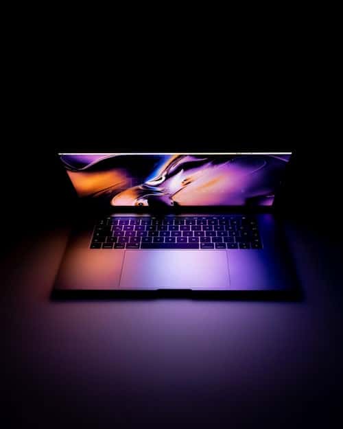 computersforschool-featureimage laptop glowing in the centre of a black room